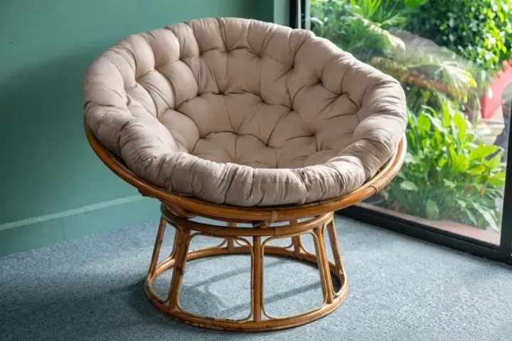 A rattan papasan chair with a tufted cushion, beside a window